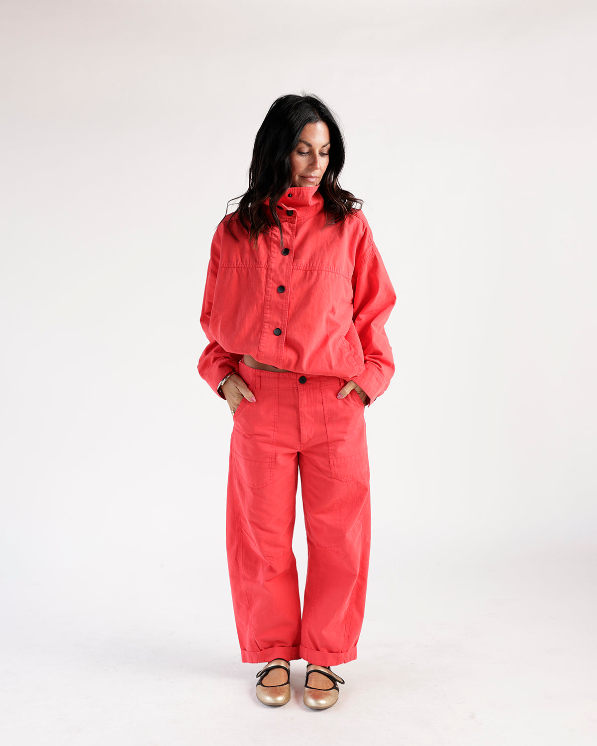 Cropped red funnel neck jacket with black buttons, worn with matching wide-leg pants