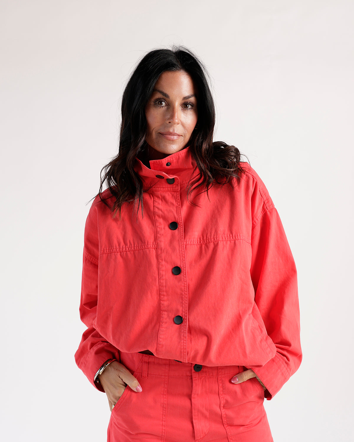 Cropped red funnel neck jacket with black buttons, worn as a matching set