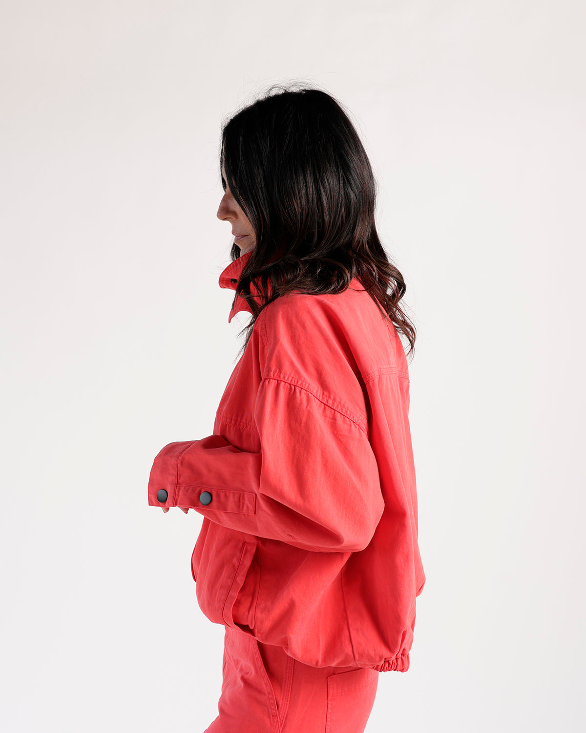 Coral red funnel neck jacket with snap cuffs, side view on model