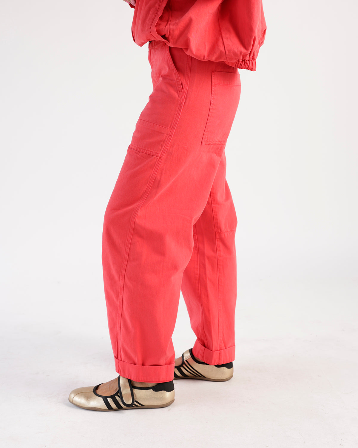 Coral red wide-leg utility pants with cuffed hems, worn with gold flat shoes.