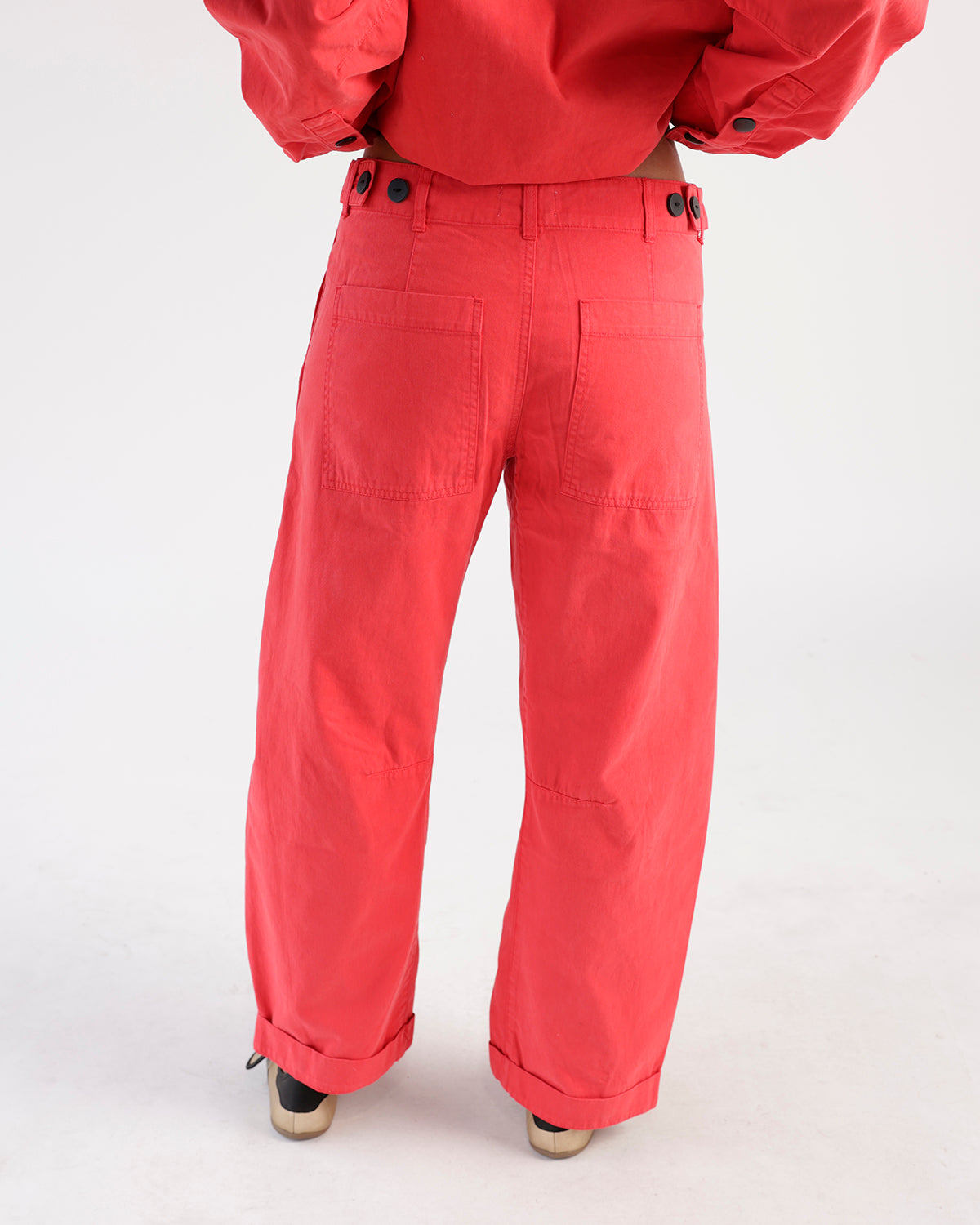 Red wide-leg utility pants with back patch pockets, black buttons, and cuffed hems