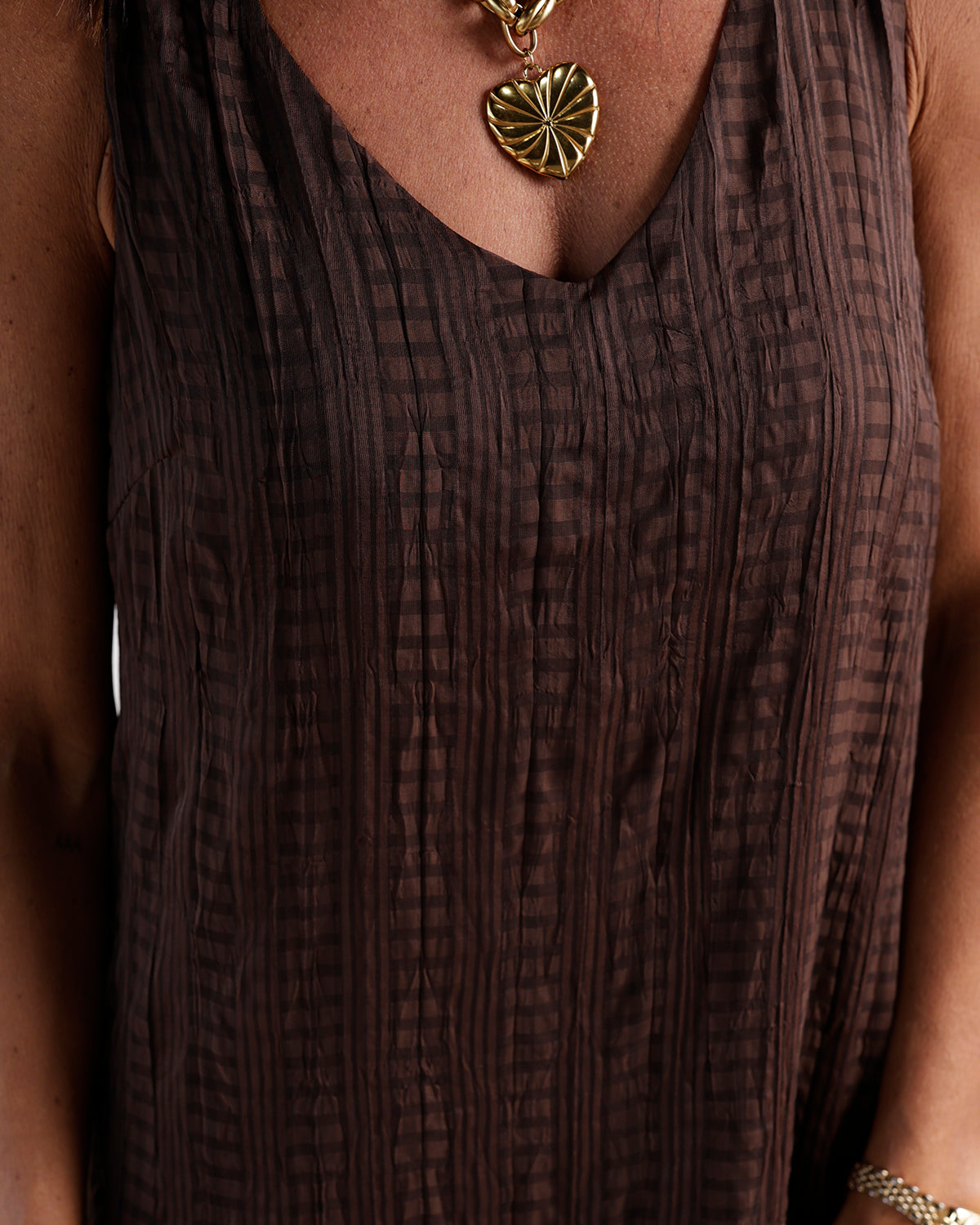 Brown plaid crinkle sleeveless maxi dress with V-neckline, worn with gold heart pendant necklace