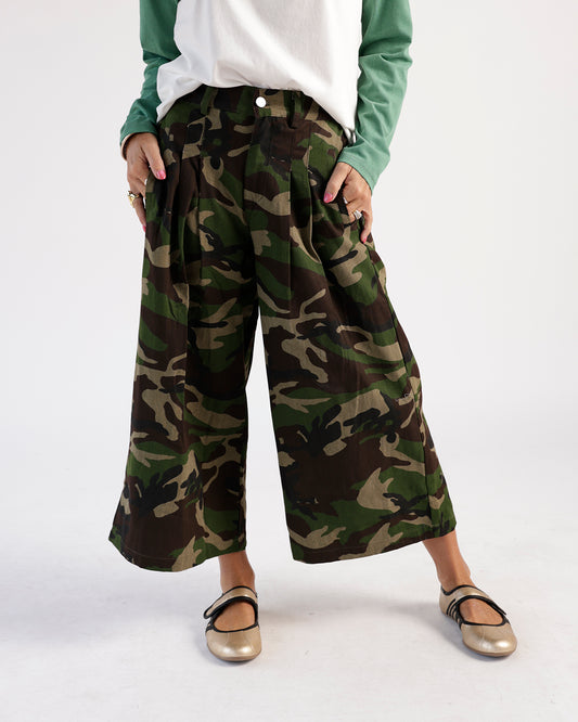 Wide-leg cropped camo pants with pleats and button waist, styled with flats.