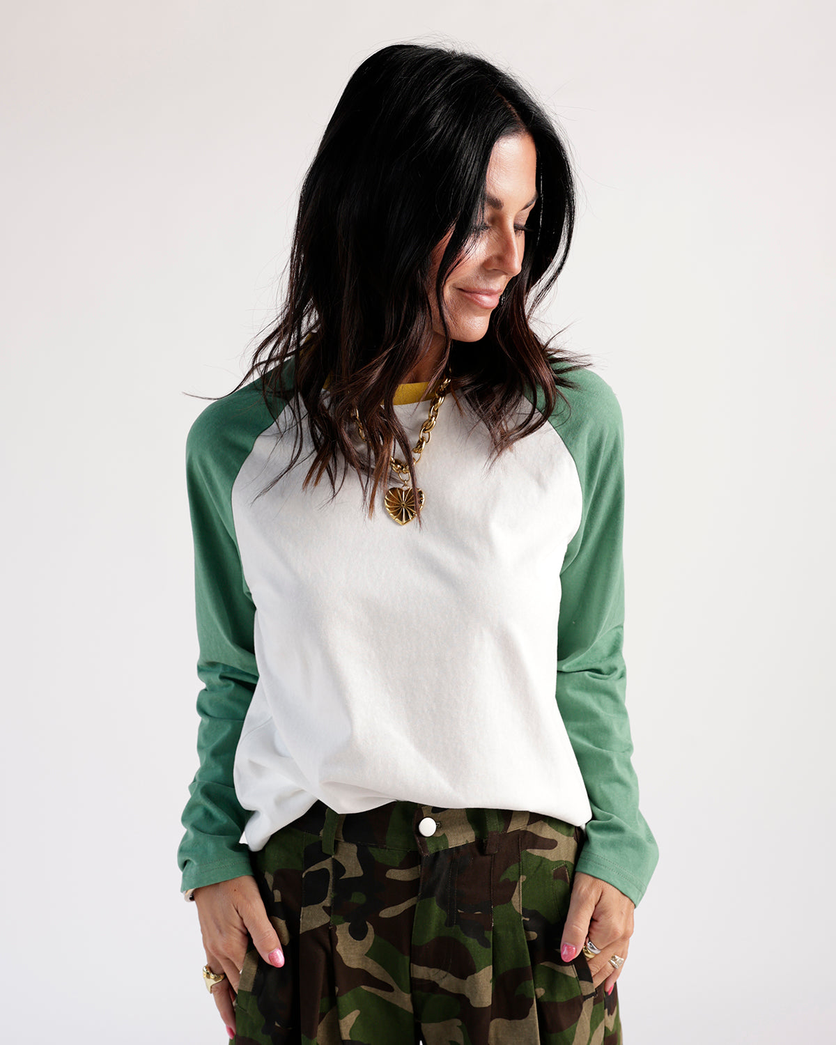 White and green raglan long-sleeve tee with yellow collar detail, worn with camo pants