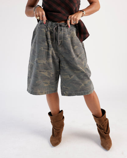 Oversized camouflage cargo shorts with drawstring waist, worn with brown suede boots.
