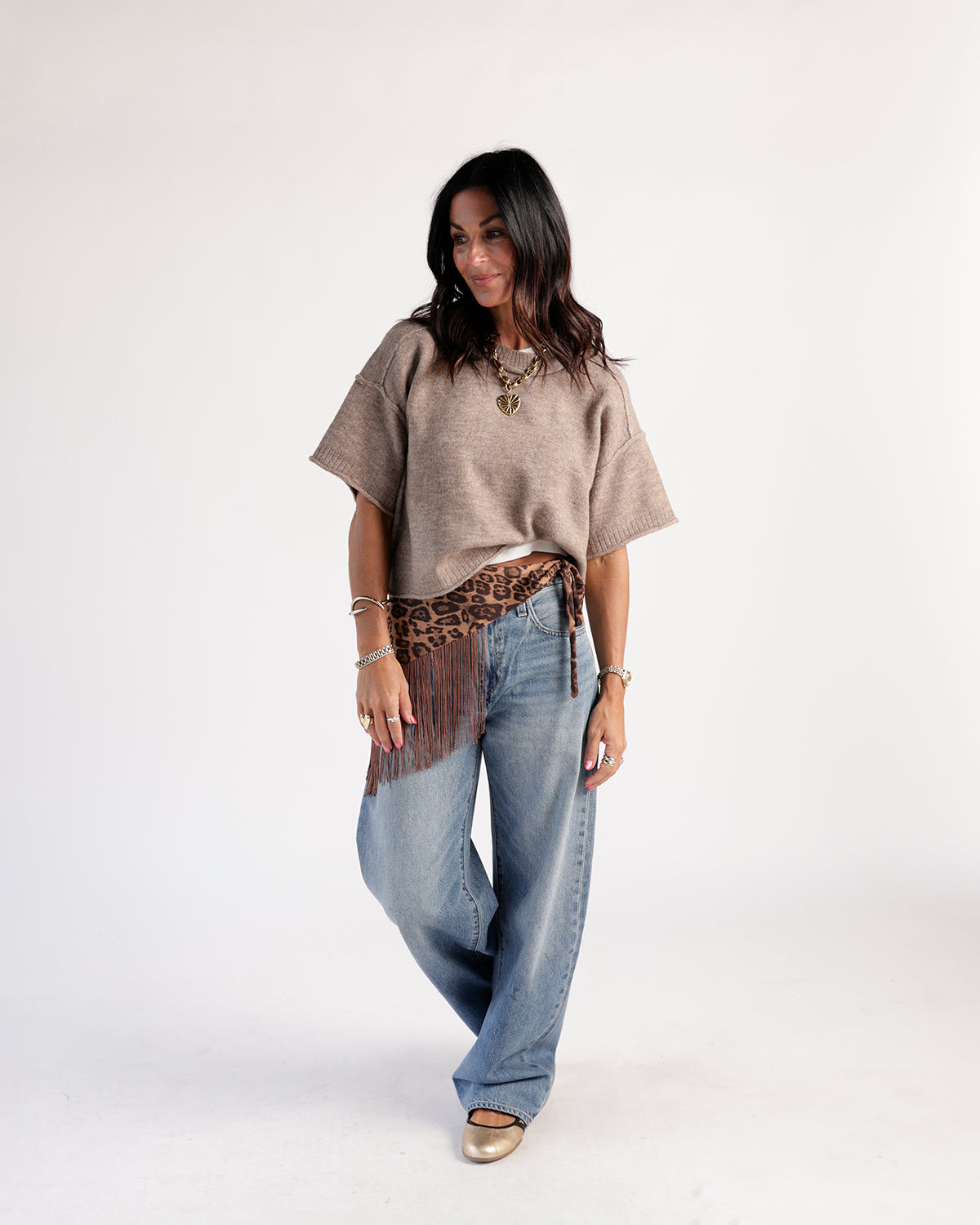 Medium wash wide-leg jeans styled with a tan knit top and leopard fringe belt
