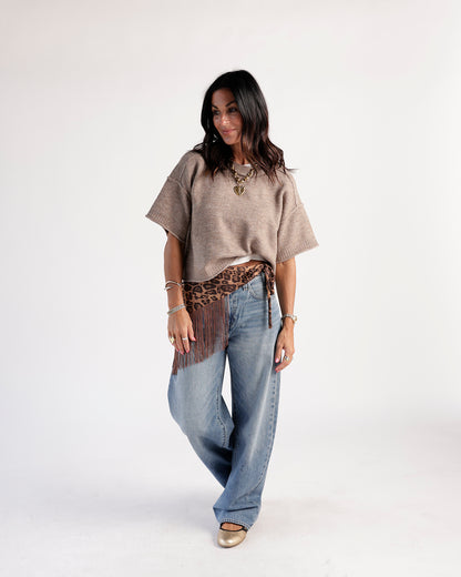 Medium wash wide-leg jeans styled with a tan knit top and leopard fringe belt