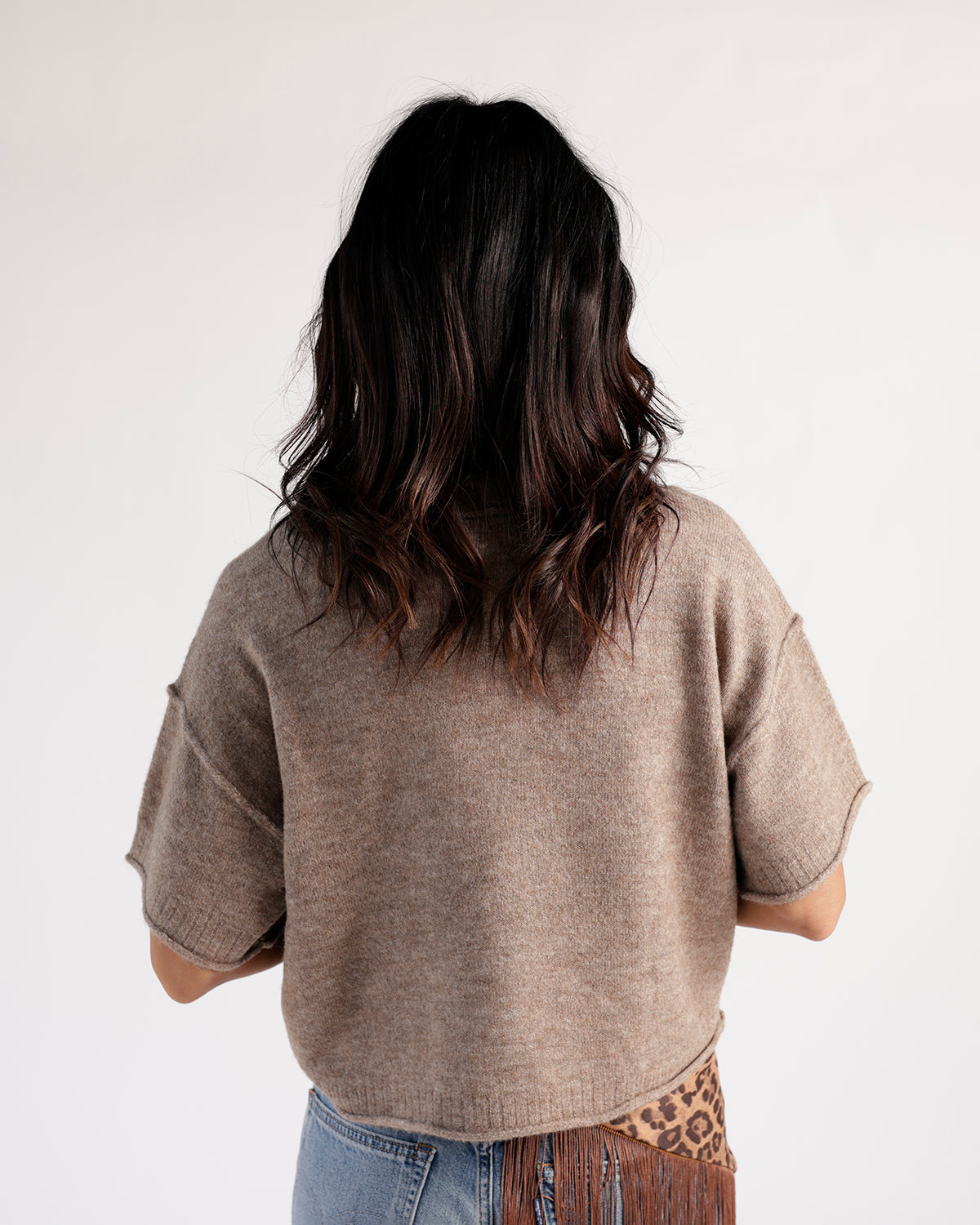 Back view of a cropped taupe short-sleeve knit sweater paired with jeans