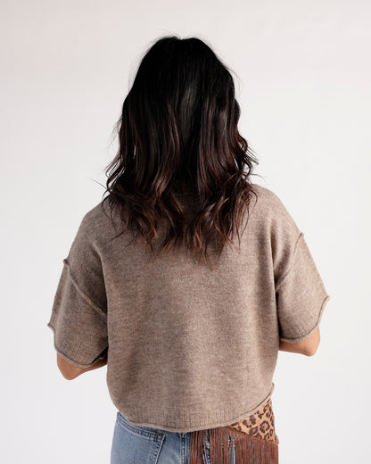 Back view of a cropped taupe short-sleeve knit sweater paired with jeans