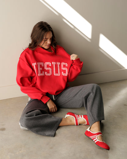girl wearing a Jesus mock neck and grey trousers sitting on the ground and wearing red athletic shoes 