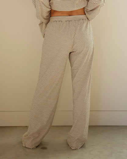 A person shown from the back wearing loose, wide-leg pants and a matching striped crop top in beige and white, standing against a plain beige wall and concrete floor.
