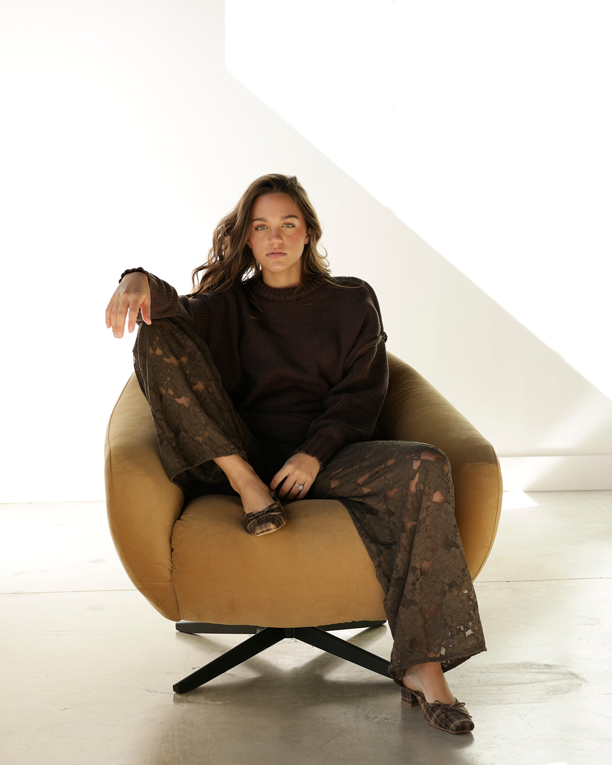 A pair of dark gray lace pants hanging on a rack, with a hand holding the hem to show the drape. A white tag with the brand name 'aren' is visible on the right side.