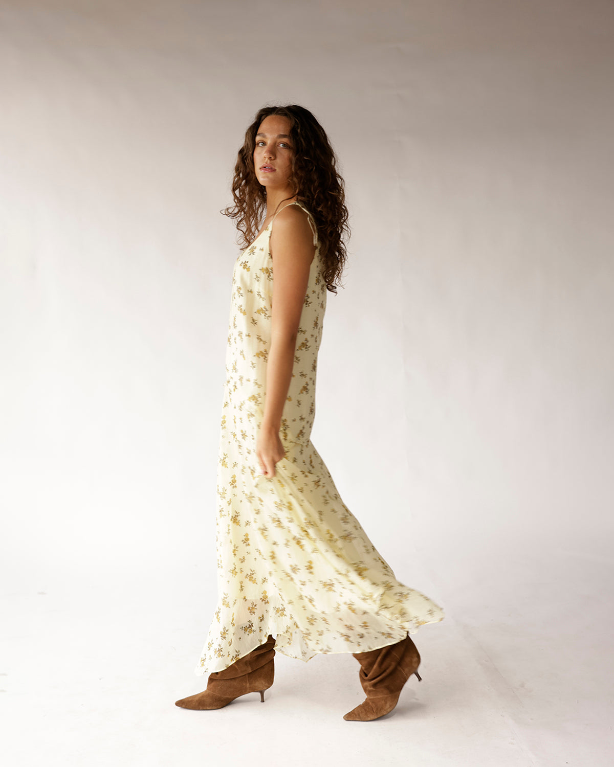 Cream floral maxi dress with thin straps and flowy skirt, styled with brown boots.