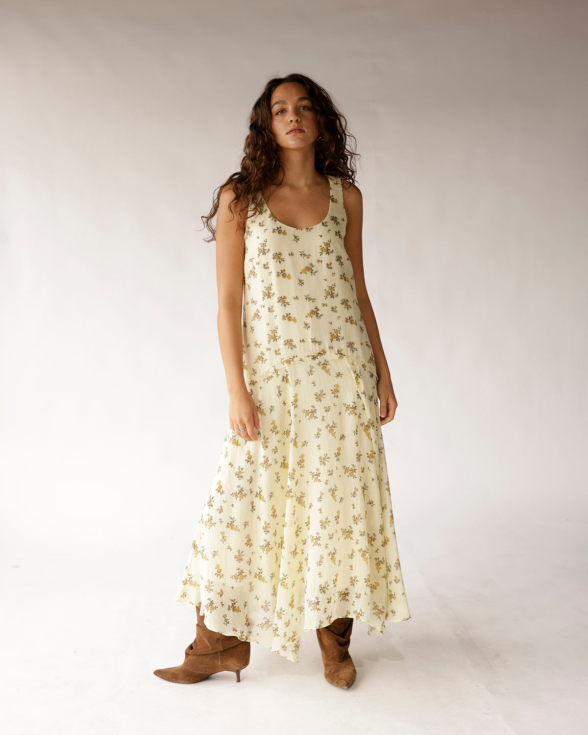 Cream floral sleeveless drop waist maxi dress with tiered skirt, worn with brown boots.
