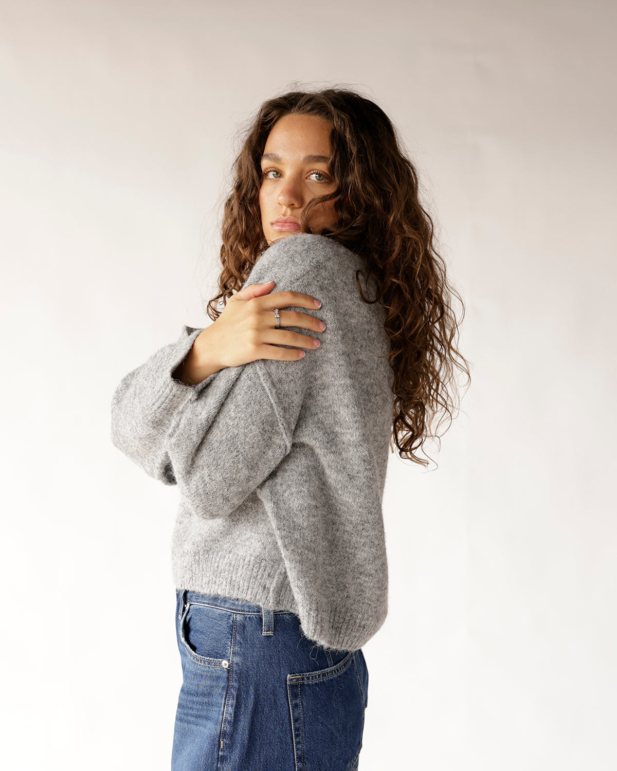 Gray heathered knit sweater with ribbed hem, worn with blue jeans, side view