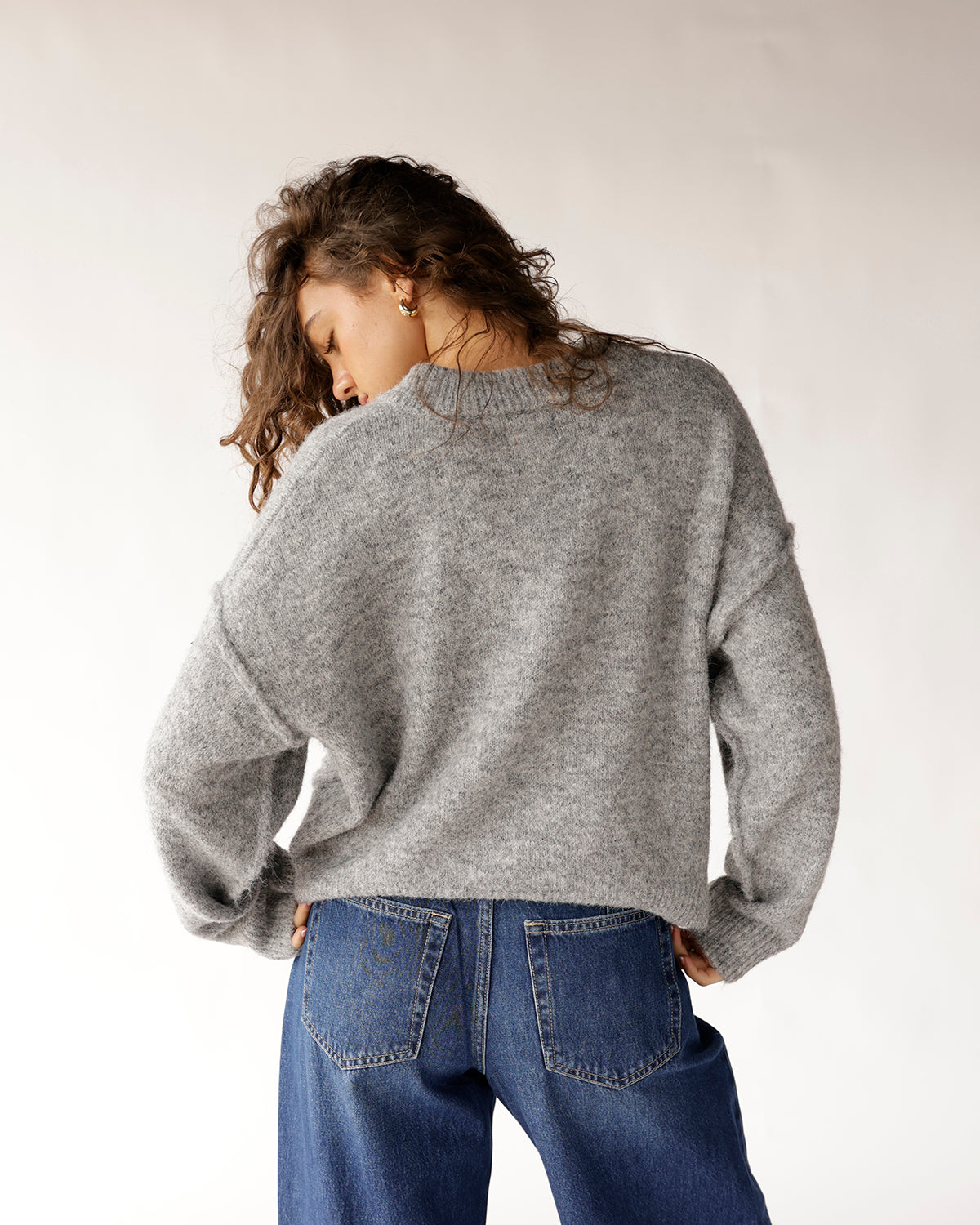 Oversized gray knit sweater with mock neck, paired with blue jeans, back view.