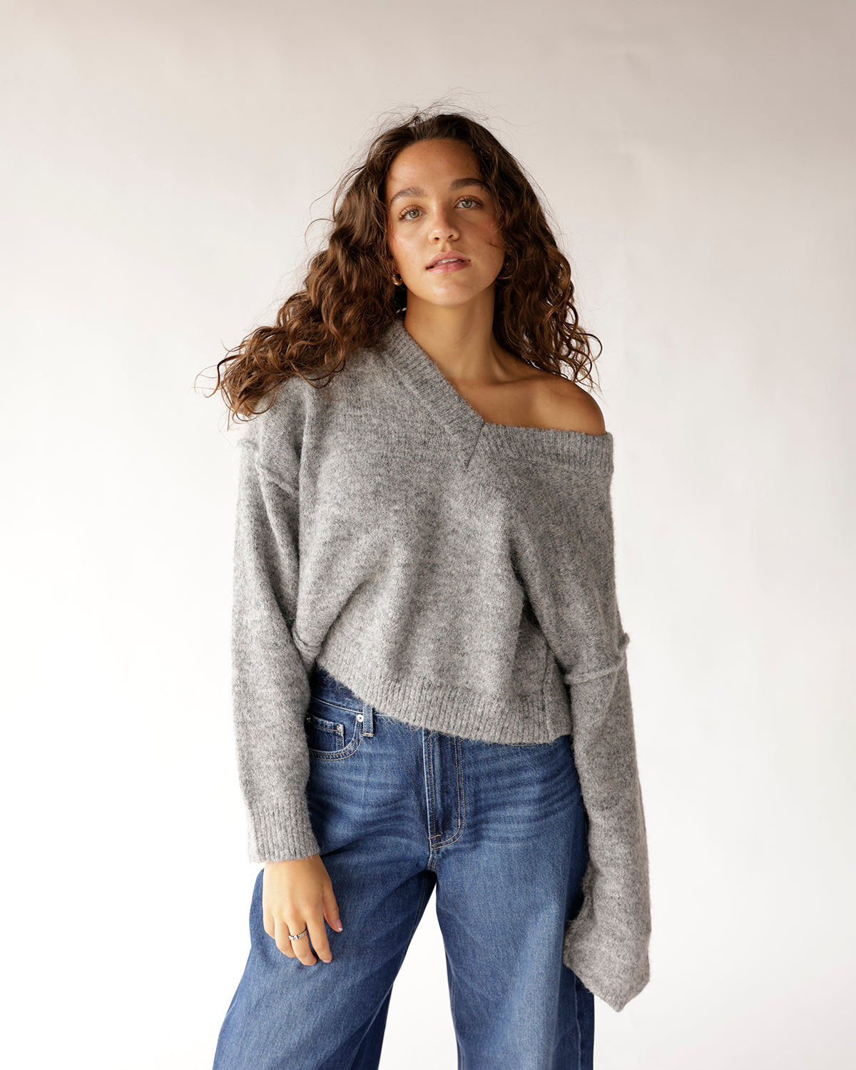 Gray oversized off-shoulder knit sweater paired with wide-leg blue jeans