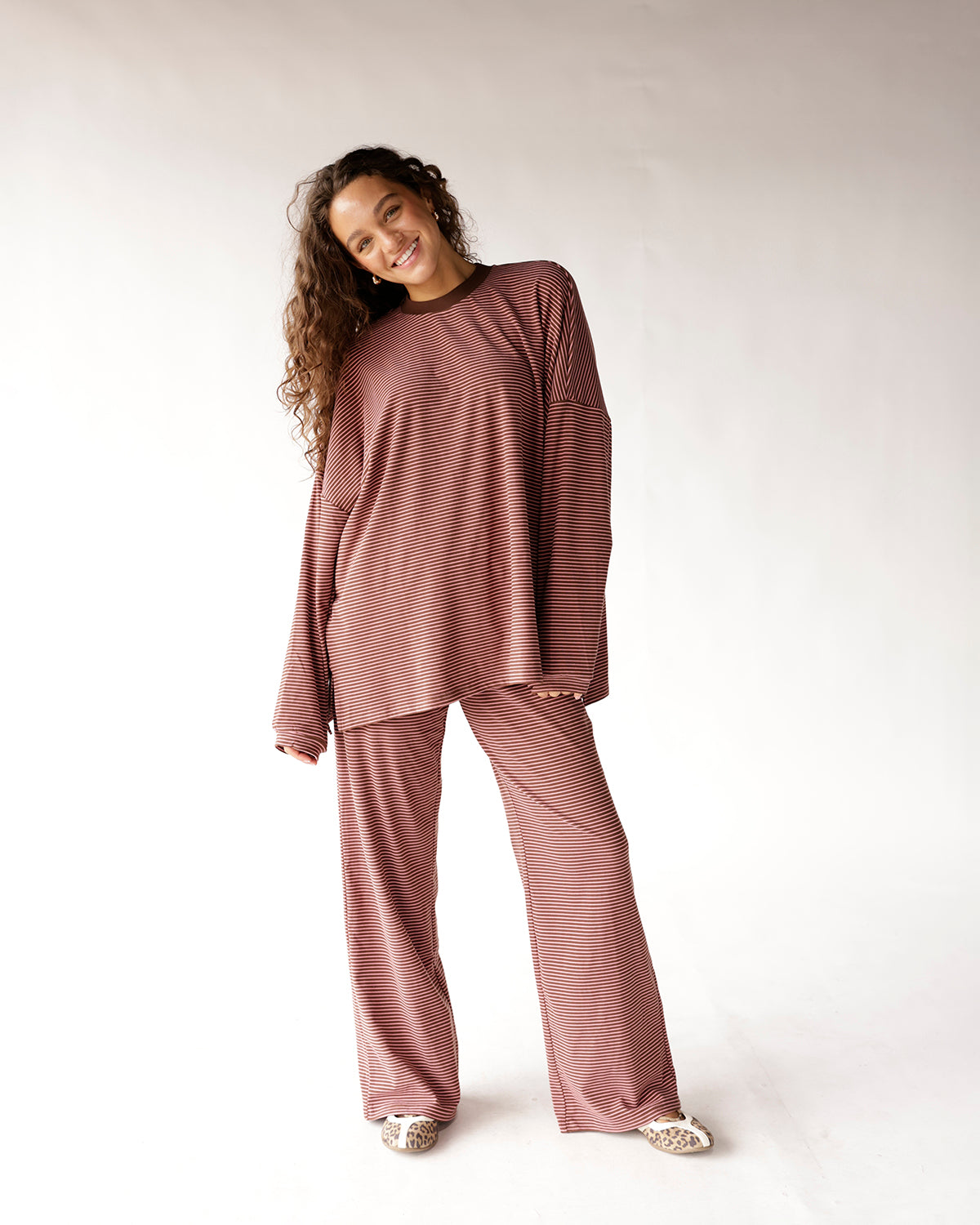 these pink and brown striped wide-leg pants are an effortless, feel-good staple you'll reach for again and again. the fine horizontal stripe pattern gives them a playful retro energy, while the smocked elastic waistband keeps the fit comfortable and relaxed. the wide, flowy leg silhouette adds a breezy, elevated touch that makes these anything but basic lounge pants. 