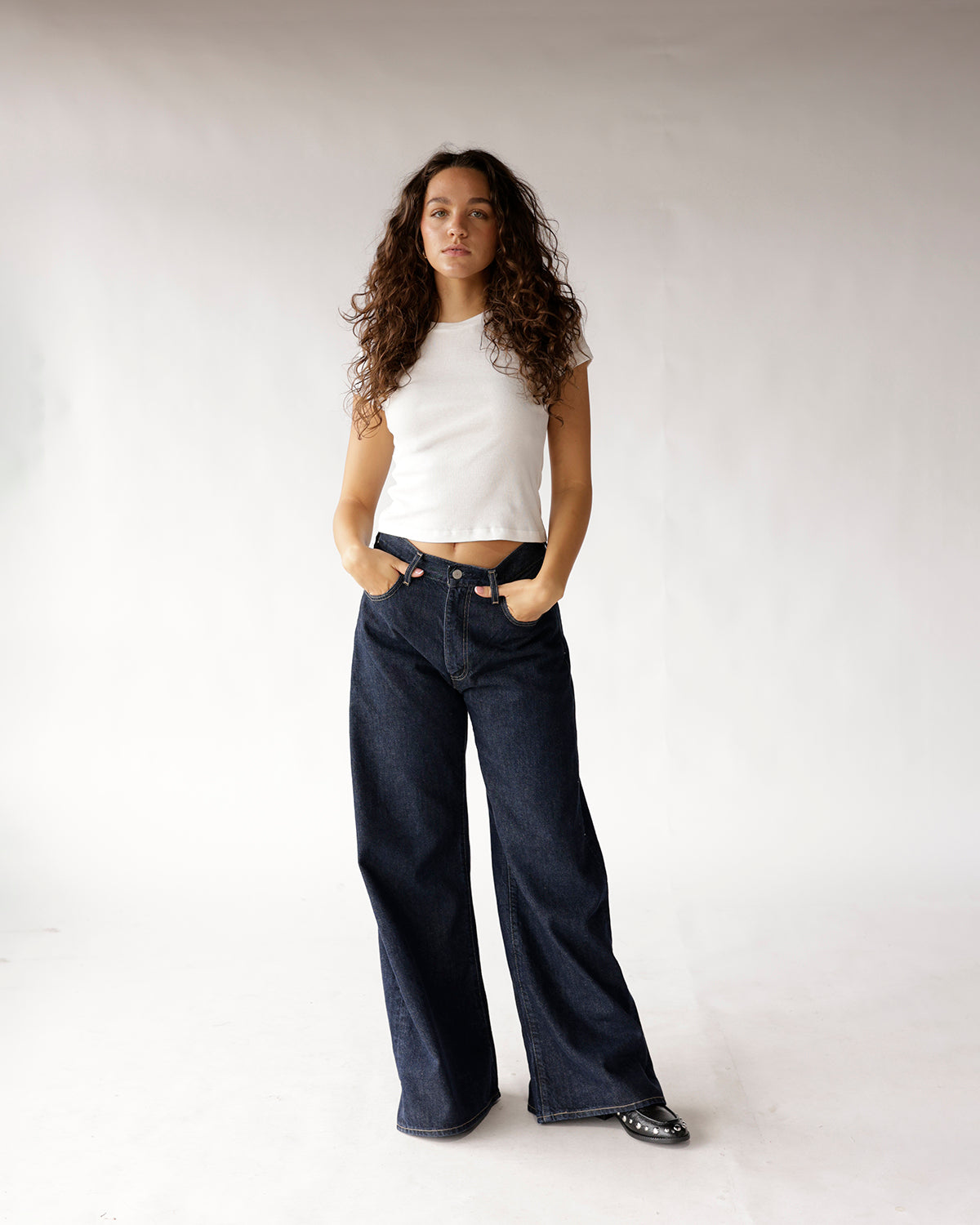 Dark wash wide-leg jeans worn with a white cropped sleeveless top and black flats.
