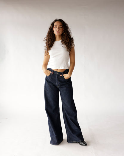 Dark wash wide-leg jeans worn with a white cropped sleeveless top and black flats.