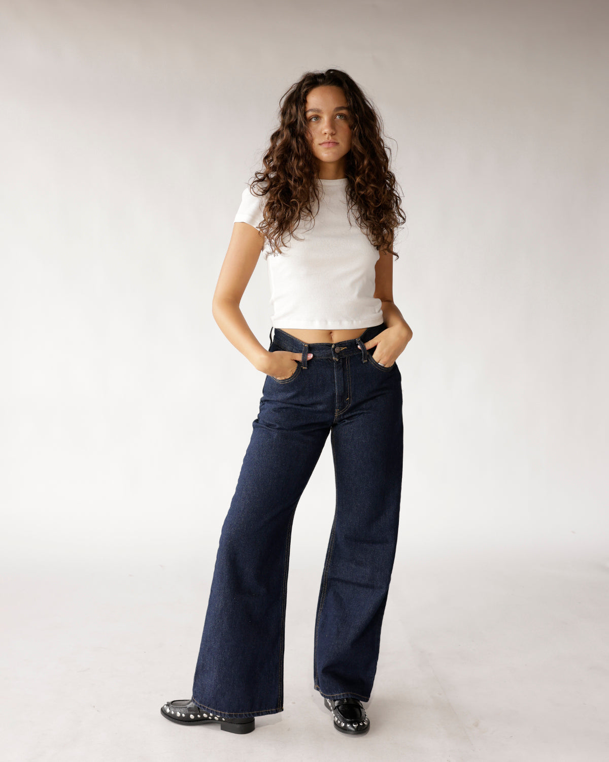 Dark indigo wide-leg boot cut jeans with contrast stitching, worn with white crop tee