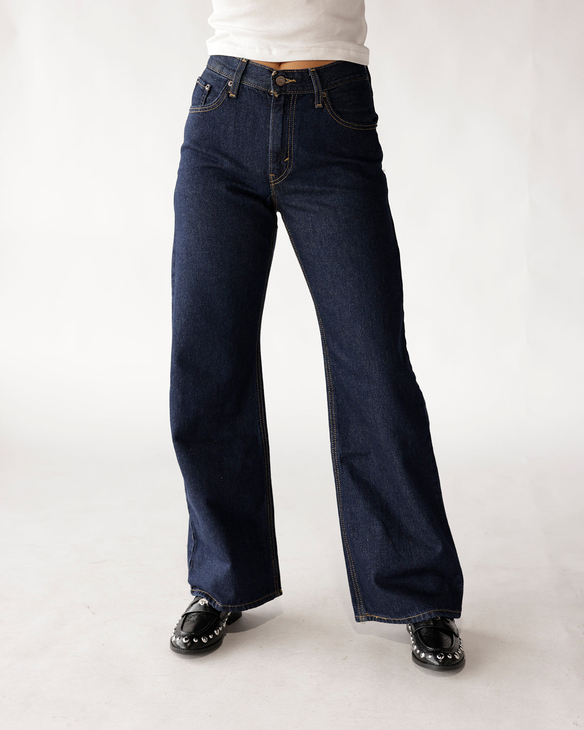 Dark indigo wide-leg boot cut jeans with contrast stitching, worn with black loafers