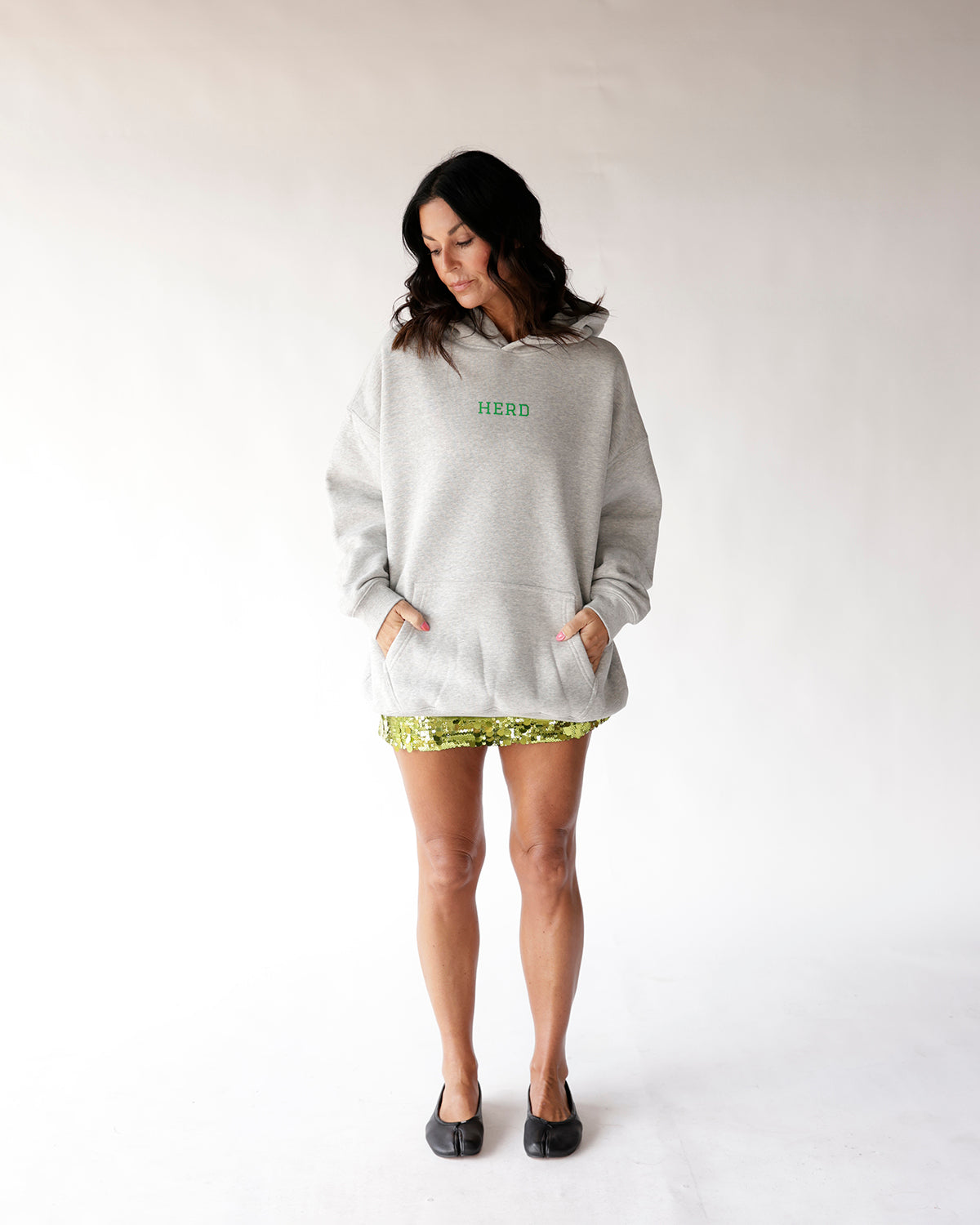 Oversized grey hoodie with green HERD text, worn over green sequin shorts