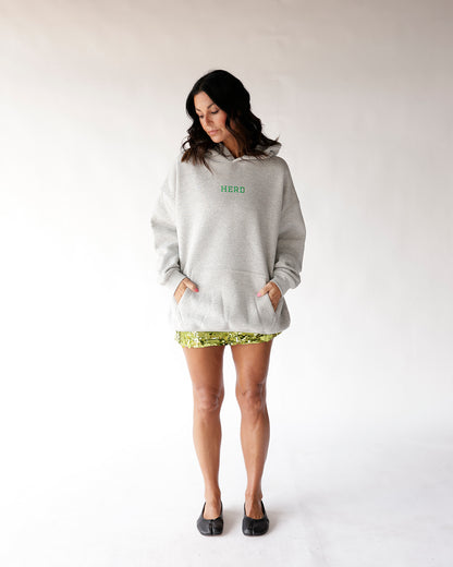 Oversized grey hoodie with green HERD text, worn over green sequin shorts