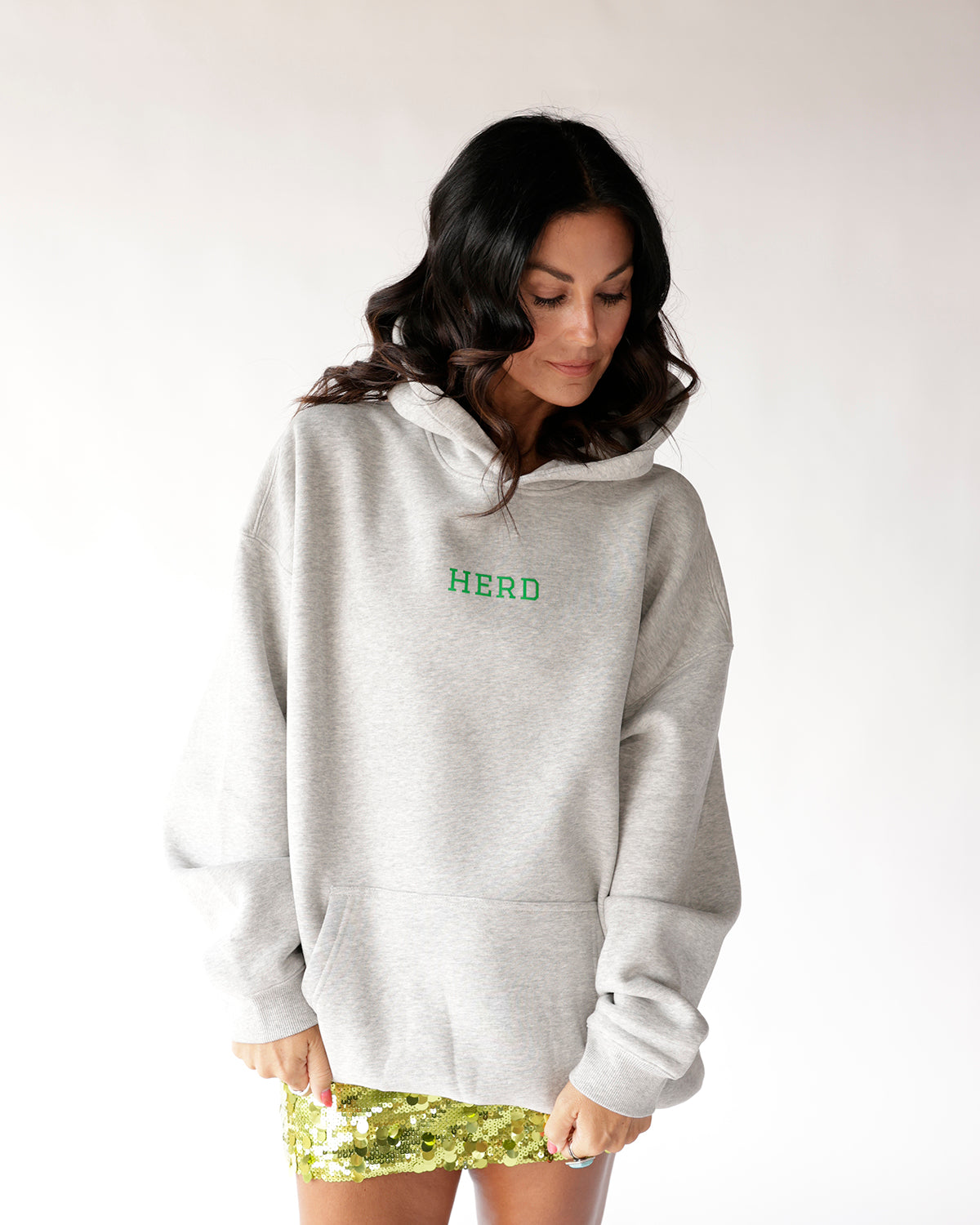 Oversized grey hoodie with green HERD graphic, worn with gold sequin mini skirt