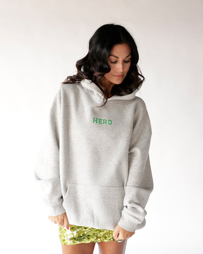 Oversized grey hoodie with green HERD graphic, worn with gold sequin mini skirt