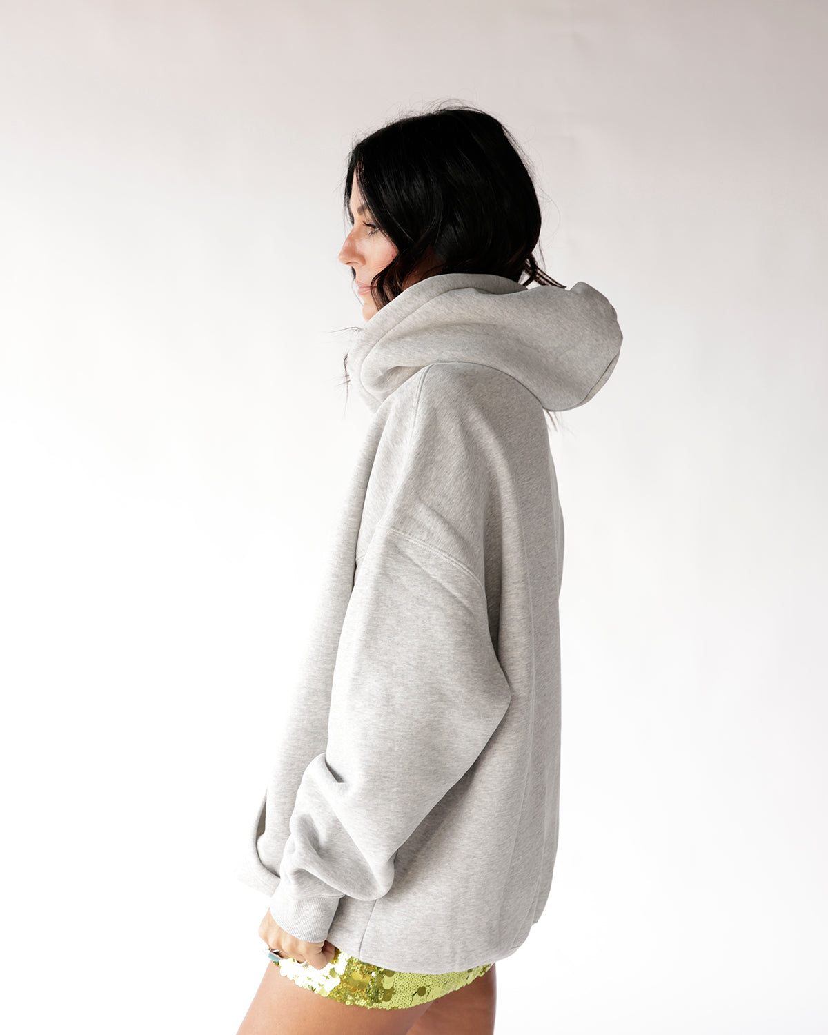Oversized grey hoodie with hood, worn with gold sequin shorts, side view.