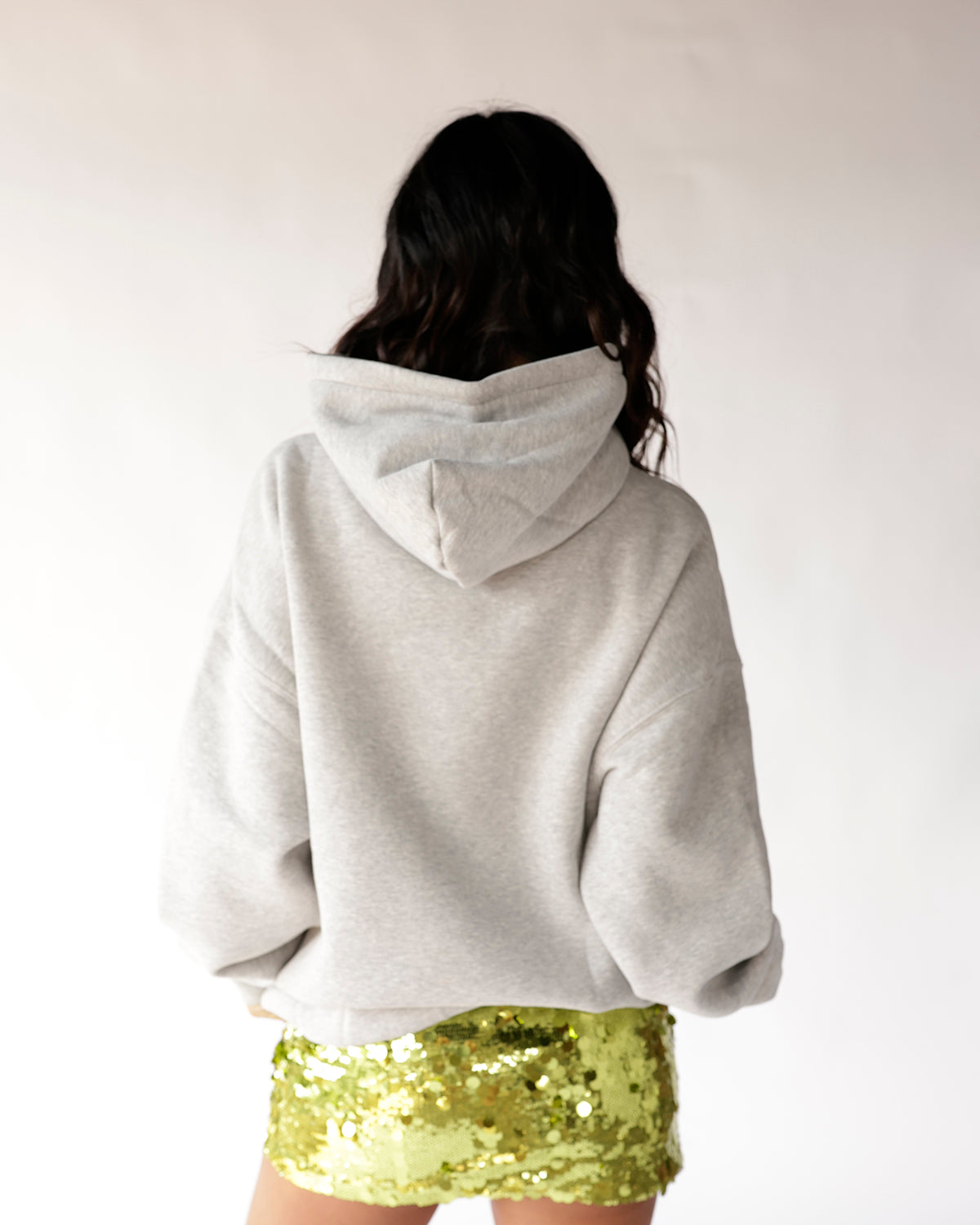Grey oversized pullover hoodie worn with yellow sequin mini skirt, back view