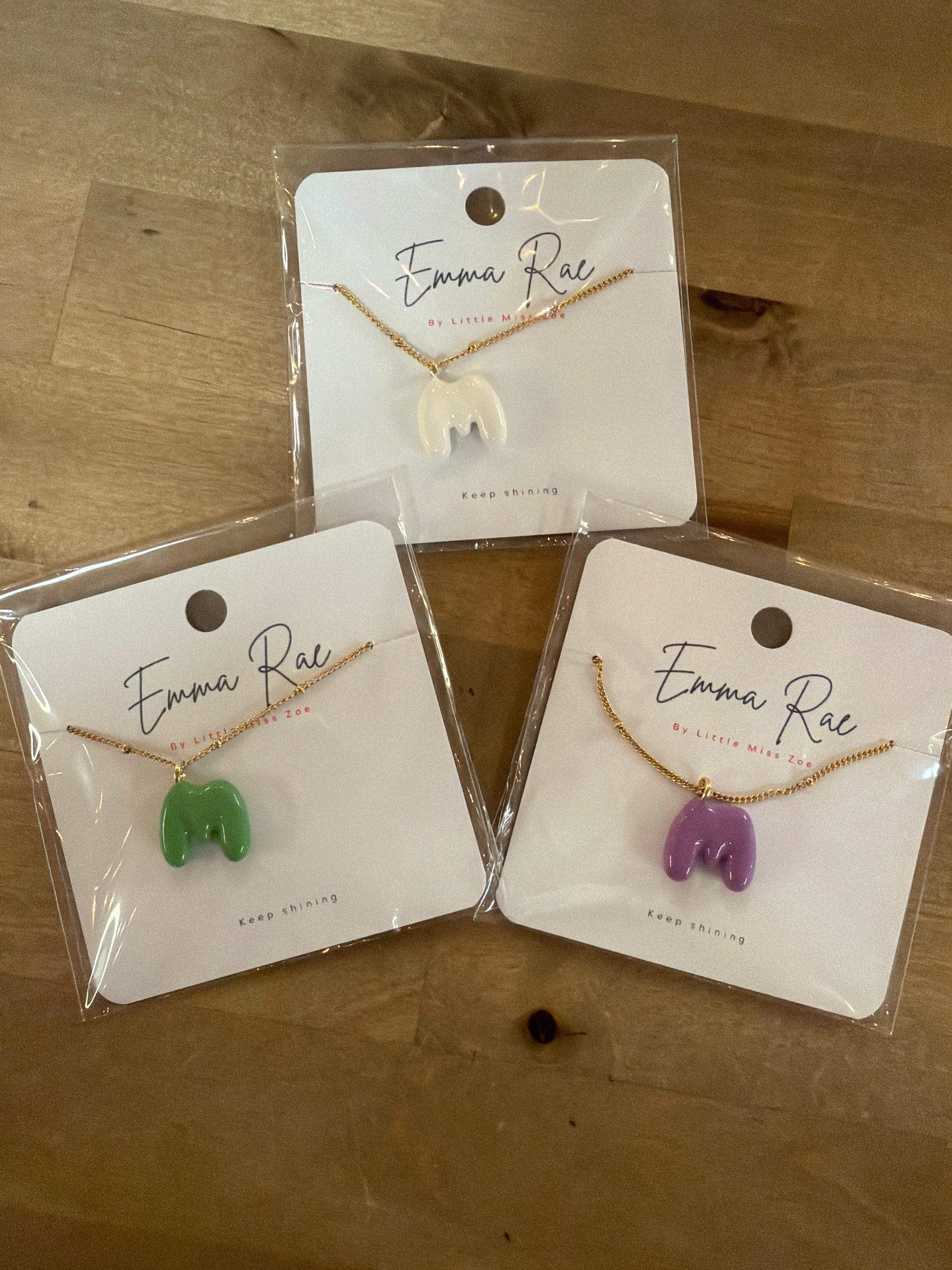 Three gold chain necklaces with bubble letter M pendants in white, green, and purple
