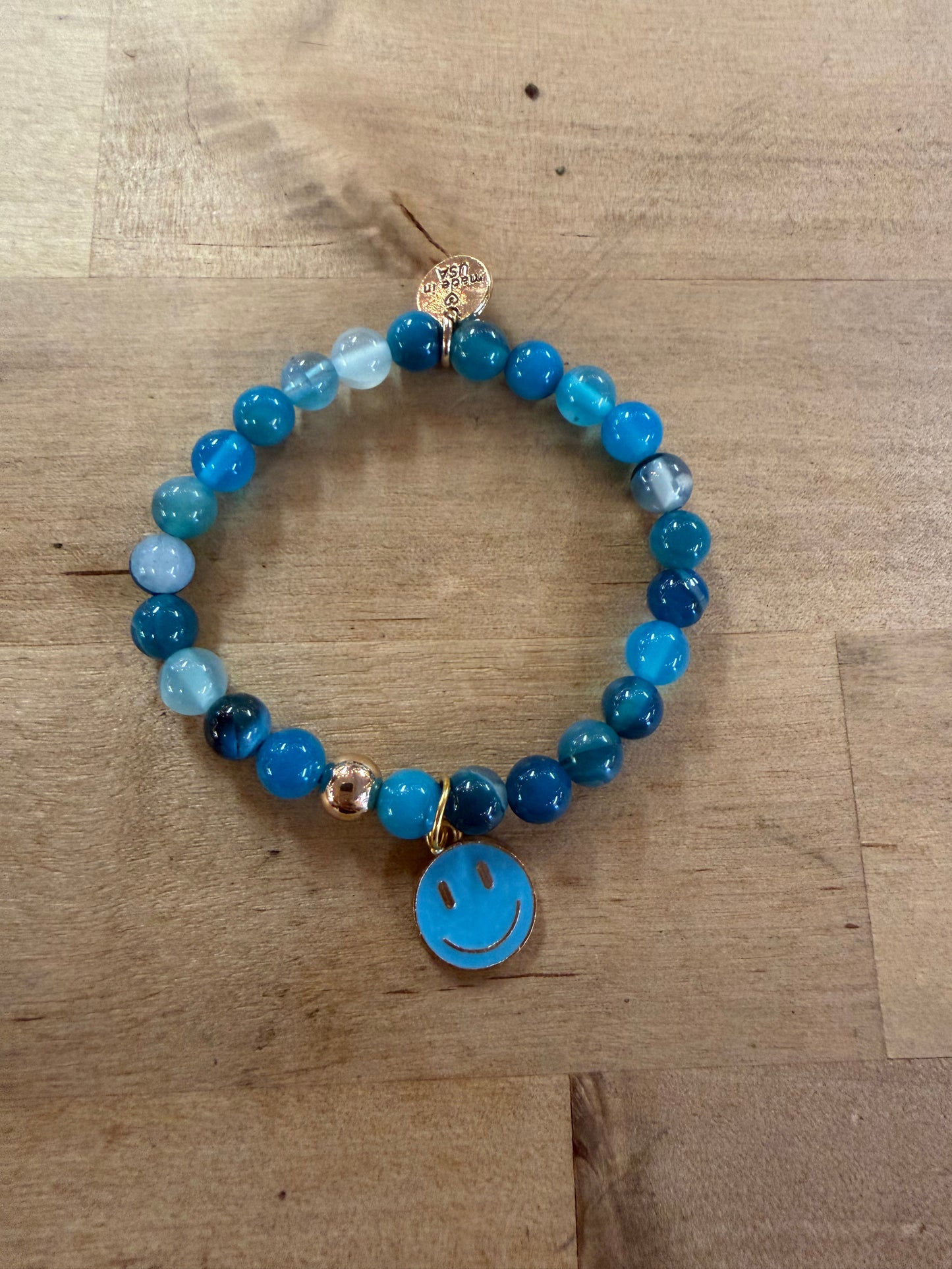 Blue beaded stretch bracelet with gold accents and blue enamel smiley face charm