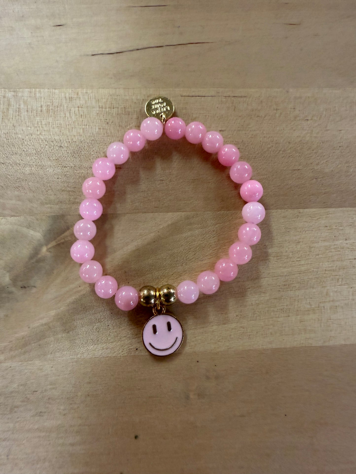 Pink beaded stretch bracelet with gold accents and white enamel smiley face charm