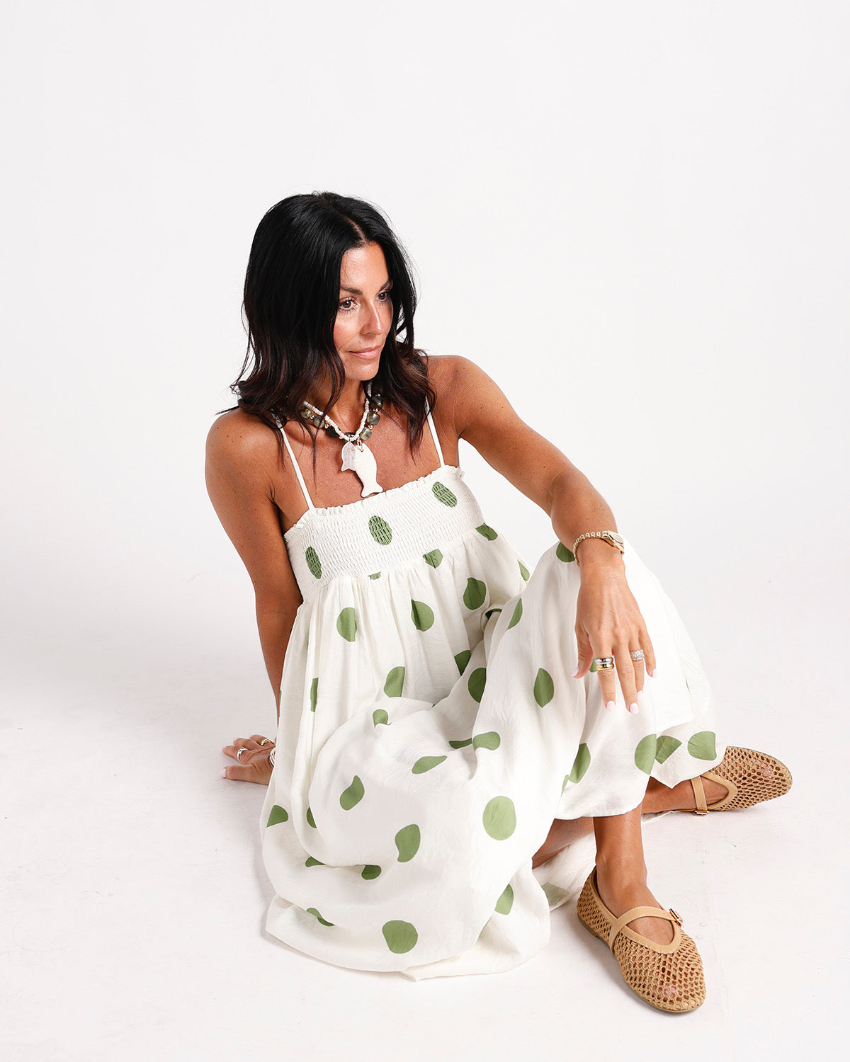White maxi dress with green polka dots, smocked bodice, spaghetti straps, worn seated.