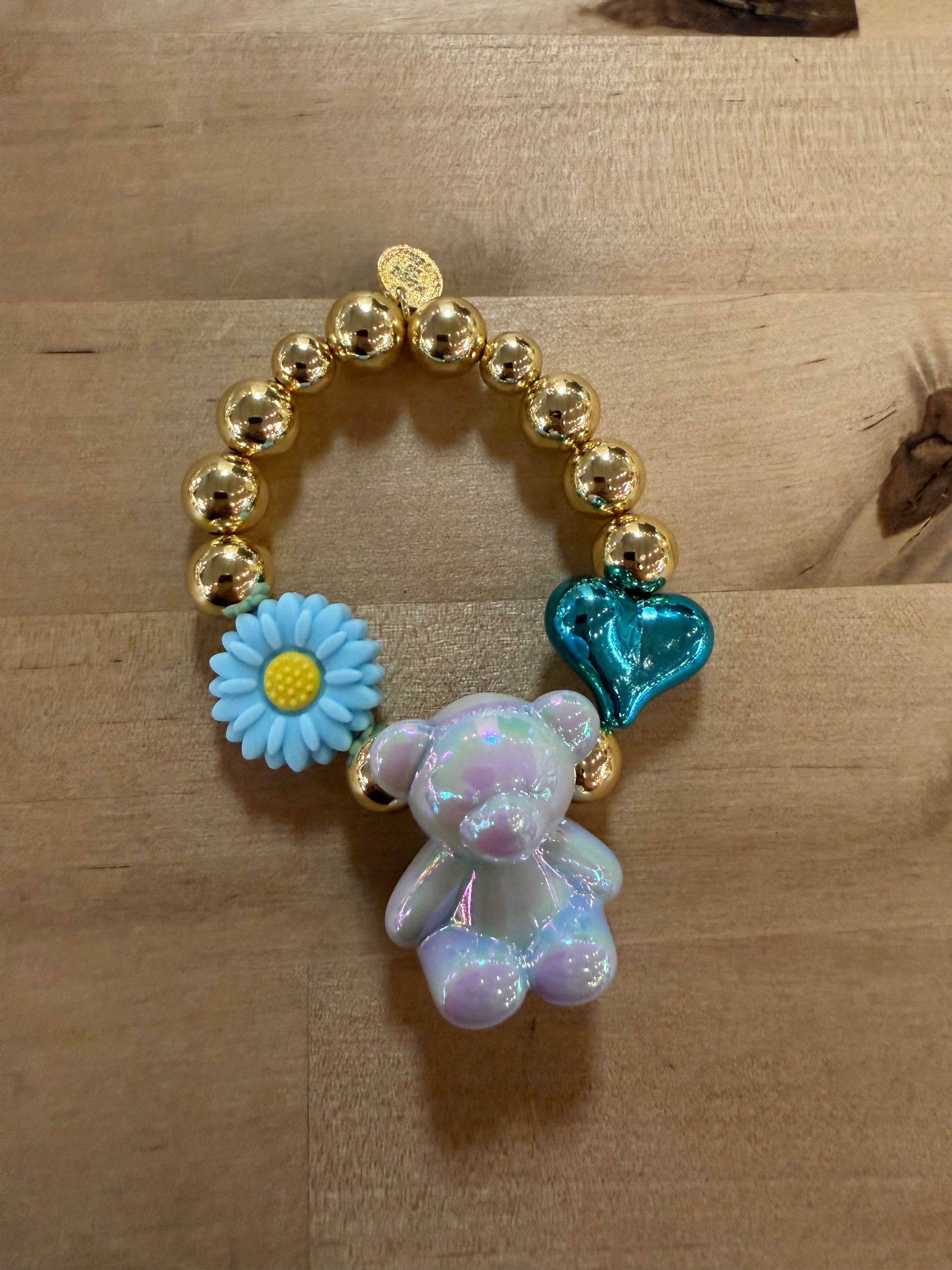 Gold beaded bracelet with iridescent bear, blue daisy flower, and teal heart charms