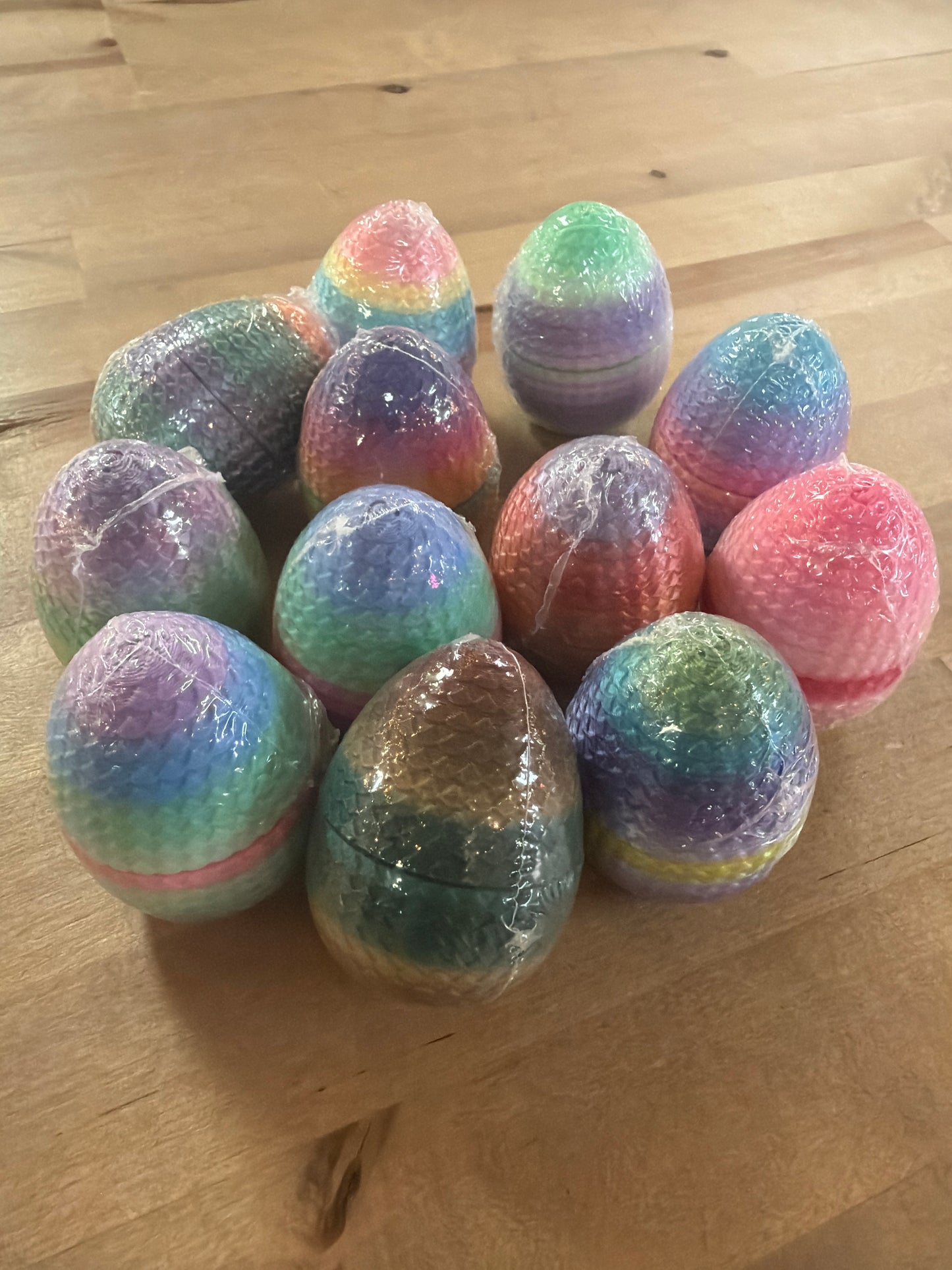 Twelve rainbow multicolor glitter dragon eggs wrapped in clear plastic on wood surface