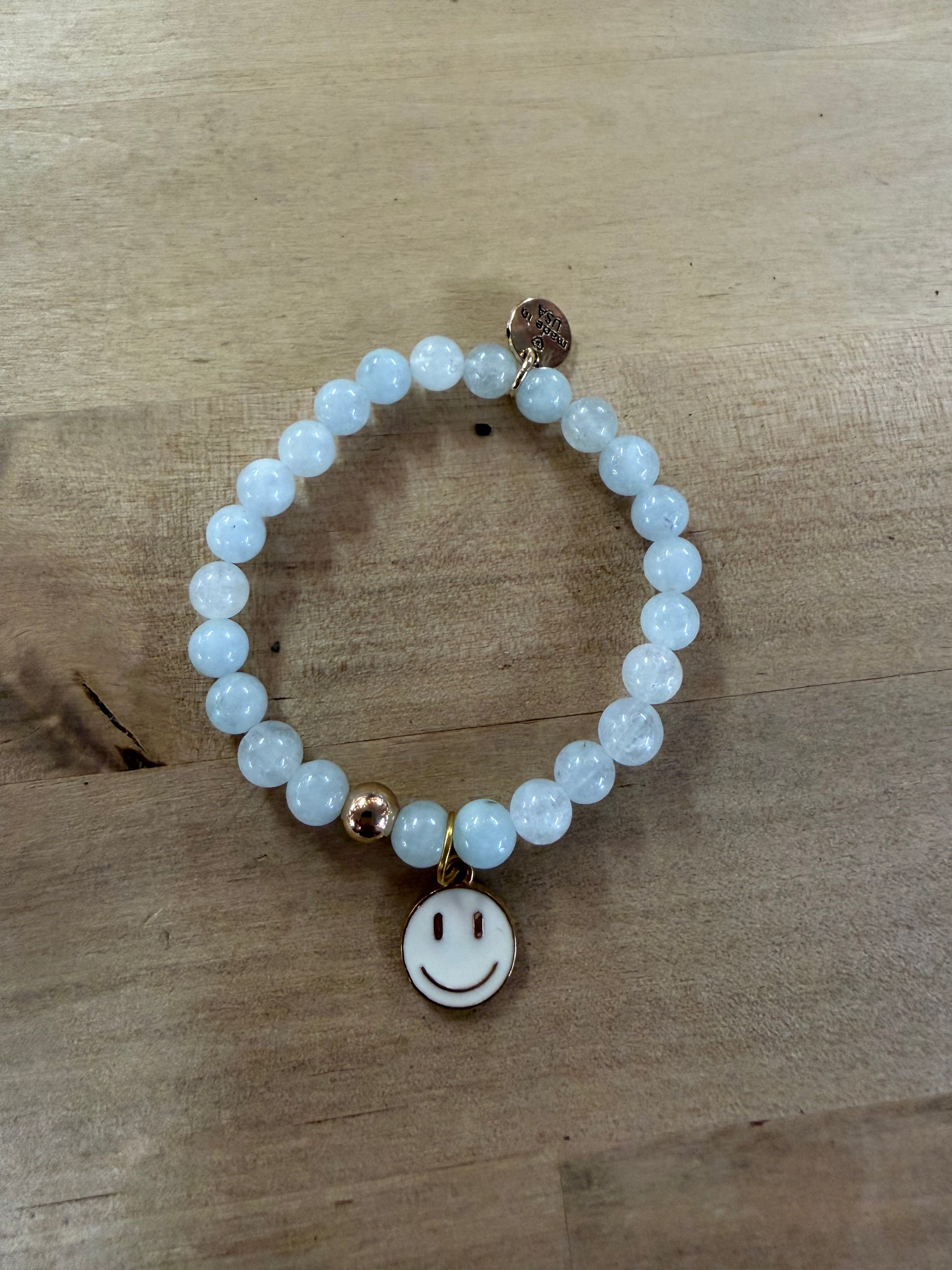 Elastic beaded bracelet with pale blue beads and gold smiley face charm