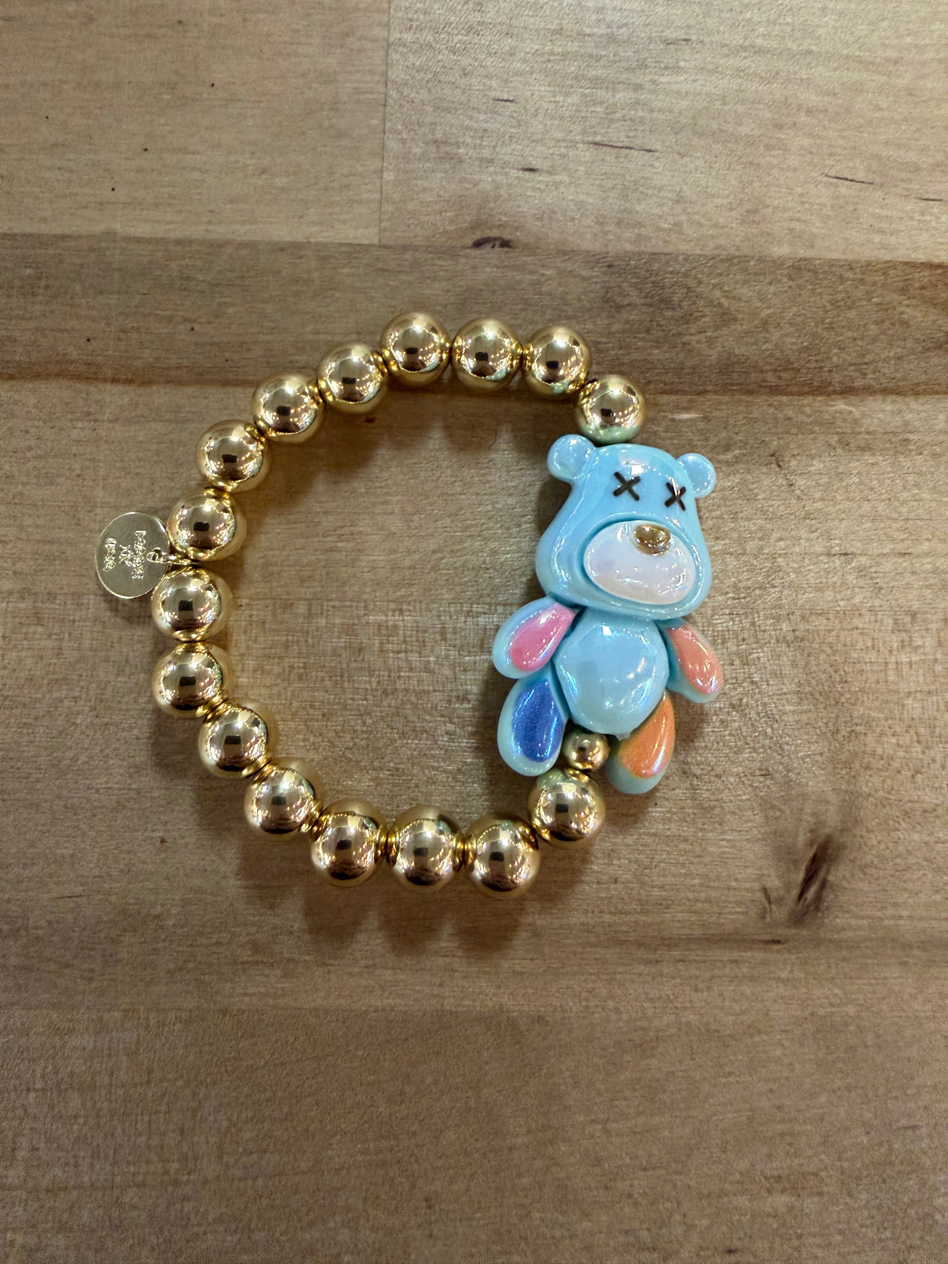 Gold beaded stretch bracelet with blue enamel bear charm featuring X eyes