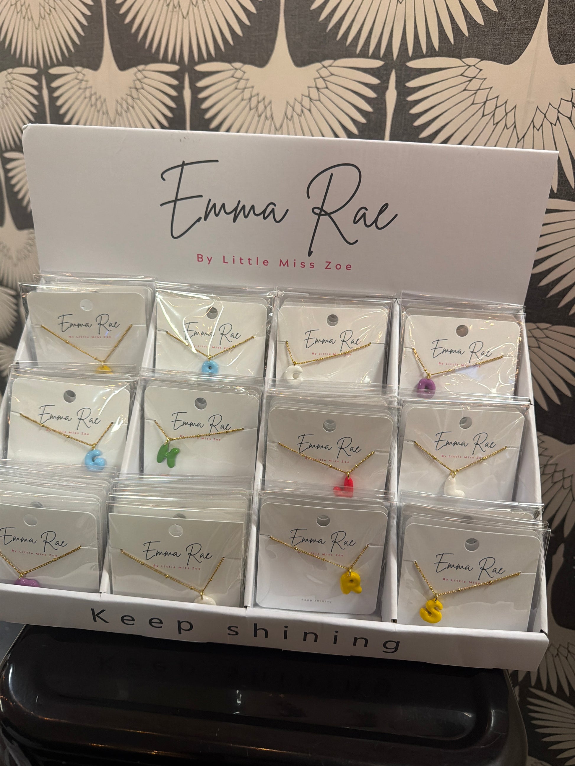 Colorful bubble initial charm necklaces on gold chains displayed in retail box