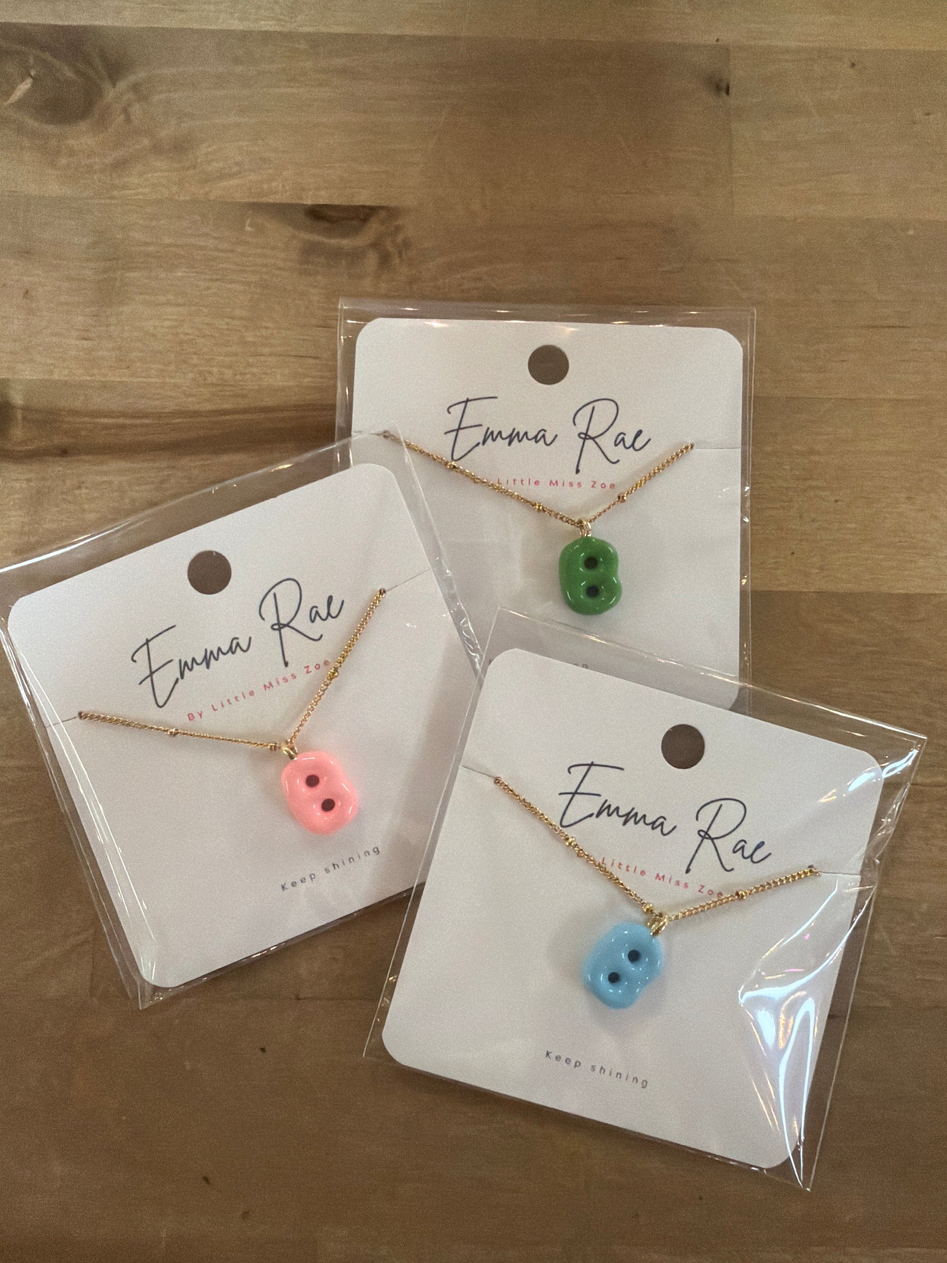 Three gold chain necklaces with colorful bubble letter pendants in pink, green, and blue