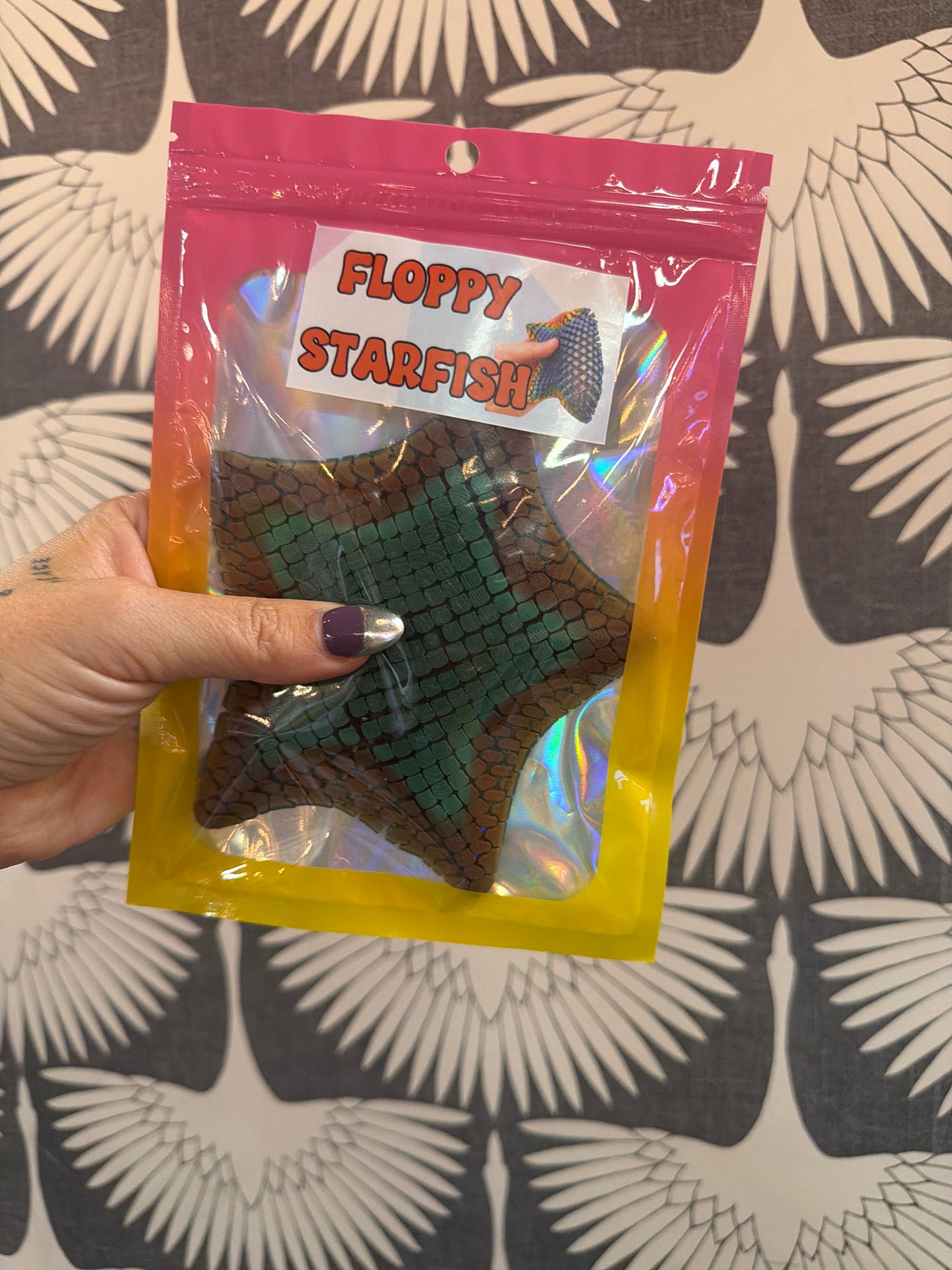 Floppy Starfish fidget toy in green and brown scale pattern, packaged in holographic bag