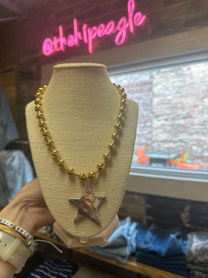 Gold beaded necklace with large silver puffed star pendant on linen bust display