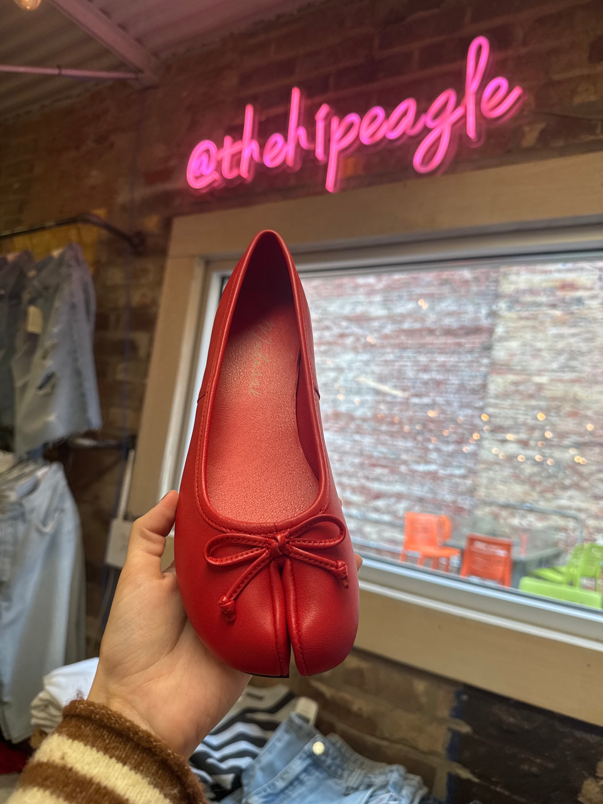 Red split-toe ballet flat with bow detail, held up in boutique