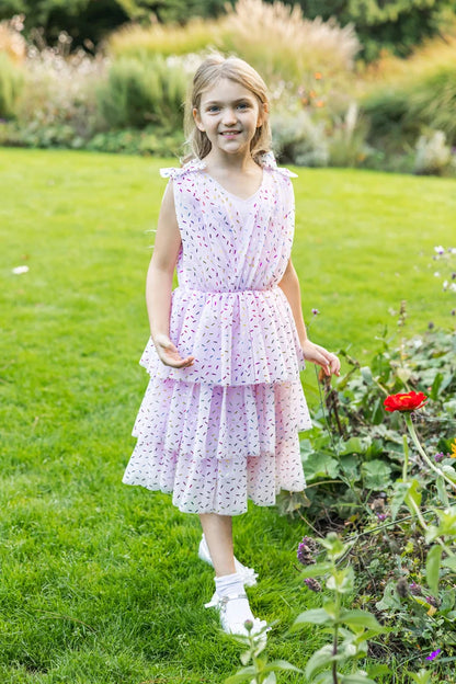 Girl wearing a pink tiered ruffle dress with colorful sprinkle print and bow straps