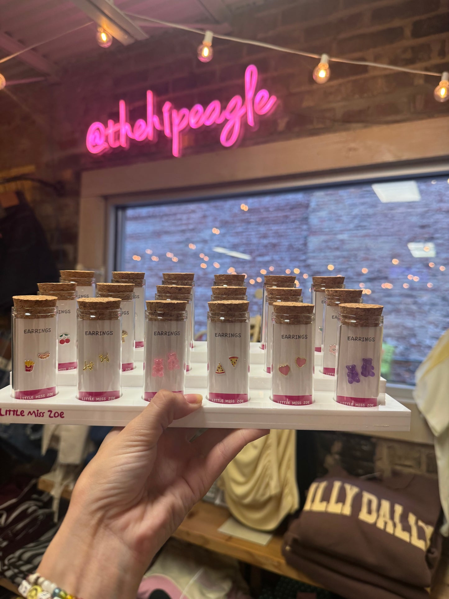 Colorful novelty stud earrings displayed in small cork-topped glass bottles on white tray