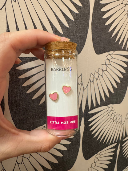 Pink heart stud earrings displayed on card inside small glass bottle with cork top