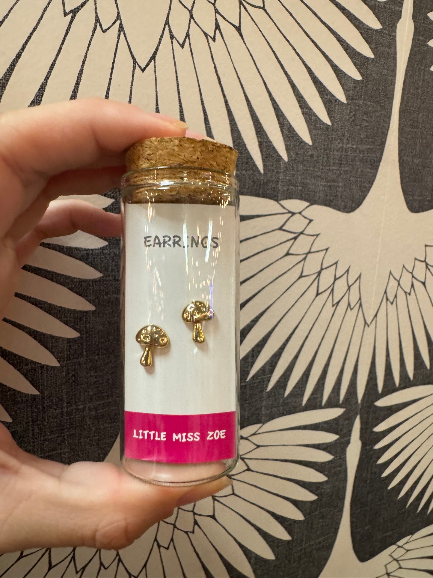 Gold mushroom stud earrings displayed on card inside small glass bottle with cork lid