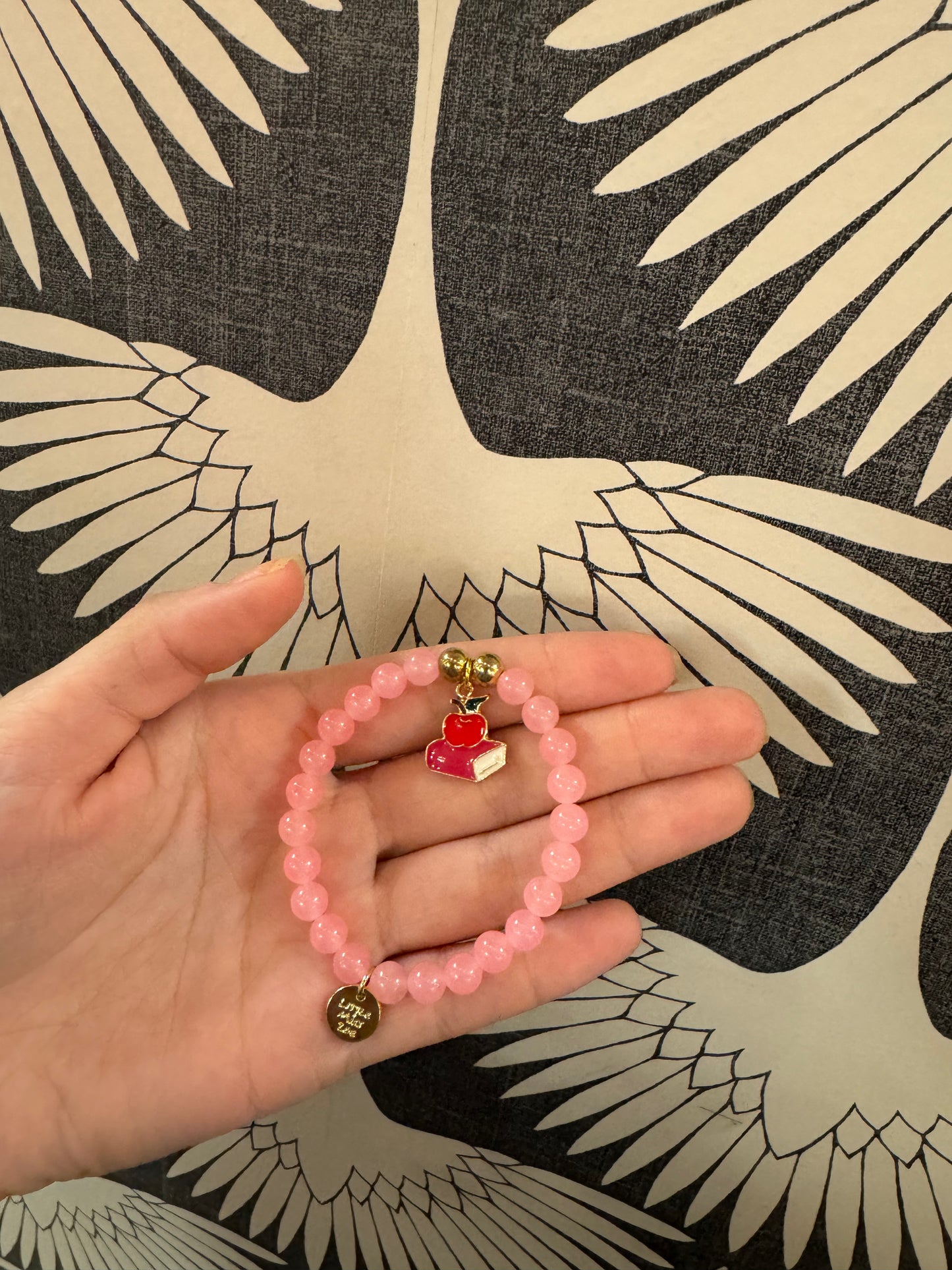 Pink beaded stretch bracelet with enamel apple and book charm, gold accents